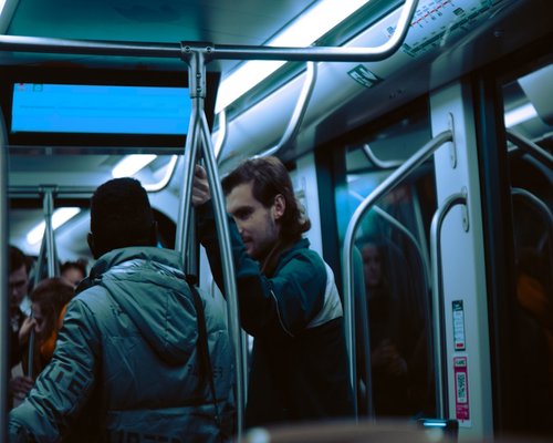 Commuter standing inside a busy transit railcar holding onto a handrail during evening rush hour